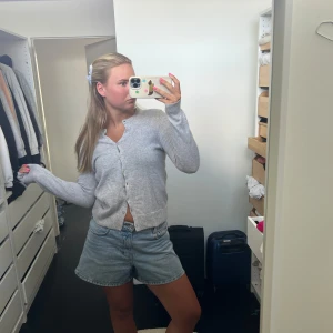 Ljusgrå kofta i kashmirblandning - Supermjuk och stilren ljusgrå kofta med rund hals och knappar framtill. Långärmad modell i kashmirblandning som är perfekt att slänga över en topp eller klänning. Ribbstickade muddar och nederkant ger en clean look. Super bra skick men knapparna är någorlunda lösa 