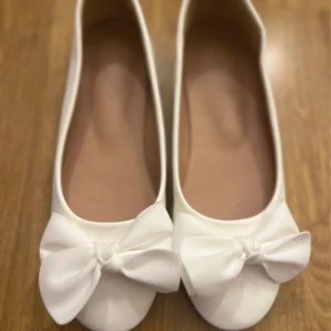 Vita ballerinaskor med rosett - Snygga vita ballerinaskor med rund tå och stora dekorativa rosetter framtill. Skorna har en klassisk och stilren design som passar perfekt till både jeans och klänning. Tillverkade i syntetmaterial för en lätt och bekväm känsla. Köp de helst på min vinted om ni har möjlighet heter samma som här