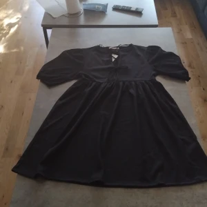 Svart kortklänning med puffärm - Svart kortklänning med puffiga halvlånga ärmar. Man kan knyta den där fram.                                    Pris kan eventuellt diskuteras.
