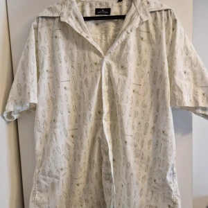 Vit kortärmad skjorta med ljusgrönt mönster från Batistini - Vit skjorta från Batistini med diskret mönster i ljusgrönt. Skjortan har korta ärmar, klassisk krage och knäppning framtill.