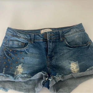 Blå jeansshorts med nitar från Denim Life - ❤️Snygga blå jeansshorts med slitna detaljer, fransig kant och coola nitar på ena sidan! MIDJEMÅTT RAKT ÖVER:34CM köp via plick🫶🏽📦