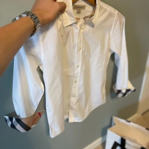 Burberry skjorta - Säljer denna riktigt fina Burberry skjortan. Denna är i mycket fint skick✨ inga större täcken på användning. Självklart äkta. Denna är i storlek (10y) runt 130-140cm. Helt perfekt för någon som är lite yngre men som ändå vill ha stil! Nypris på denna ligger runt 2900kr, säljs för 450