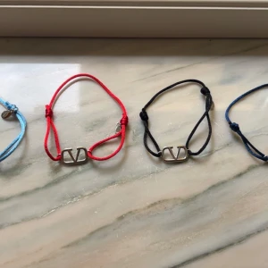Valentino armband i olika färger - Säljer flera snygga armband från Valentino med justerbart band i rött, svart, blått och ljusblått. Varje armband har en silverfärgad metallbricka med det ikoniska V-logotypen. Perfekt accessoar för att lyfta din stil. Svarta 500kr, mörkblå 450, ljusblå 350, röda 300. Kvitto finns för alla 