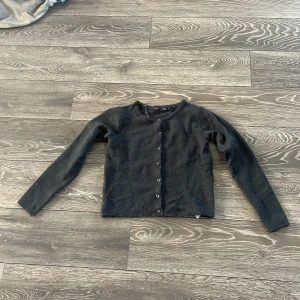 Mörkgrå kofta från 157, XS - Mysig mörkgrå kofta från 157 i stickat material. Klassisk rund halsringning och knäppning framtill med små knappar. Perfekt att slänga över en t-shirt eller linne. Långärmad och enkel att matcha till olika outfits.