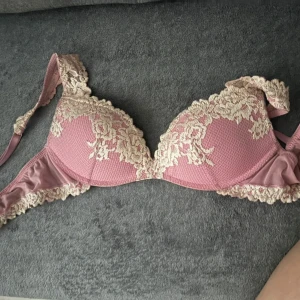 Rosa spetsblus med broderade detaljer - Supersöt rosa blus med krämvit spets och broderade blommor. Den har vadderade kupor och breda axelband med spetskant. Perfekt för dig som gillar romantisk och feminin stil. Materialet är mjukt och stretchigt för extra komfort.