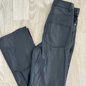 Svarta skinnbyxor från Zara - Snygga svarta byxor i skinnimitation från Zara med klassisk femficksdesign och silverfärgade detaljer. Byxorna har hög midja och raka ben😊 De är möjligtvis använda någon enstaka gång. Storlek 34