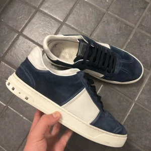 Valentino Flycrew (Byten går fint) - Snygga Valentino Flycrew sneakers i mörkblå mocka och vitt skinn. Skorna har svarta snören, coola nitar på hälen och kamouflagemönstrad sula. Perfekta för dig som vill sticka ut med exklusiva detaljer och streetkänsla. Rabatt om man följer ✅ Byten går fint men skickar ej först 🤝