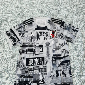 Japan fotbollströja Tokyo-motiv Adidas - Unik Japan fotbollströja från Adidas med svartvita Tokyo-inspirerade motiv och japanska tecken. Tröjan har korta ärmar, rund hals och klassiska Adidas-ränder på axlarna. Materialet är lätt och andas, perfekt för match eller träning.