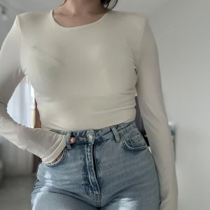 Beige långärmad topp i mesh - Säljer en stilren beige långärmad topp i tunn mesh med rund halsringning. Sitter tight och har en clean look som passar perfekt till jeans eller kjol. Materialet är lätt och stretchigt, vilket gör den superbekväm och enkel att styla.