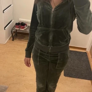 Juicy Couture grön velourjacka XS - Mörkgrön velourjacka från Juicy Couture i storlek XS. Jackan har huva, dragkedja framtill, snörning och ribbade muddar. Perfekt för en chill och trendig look, med klassiska Juicy-detaljer och skön passform.
