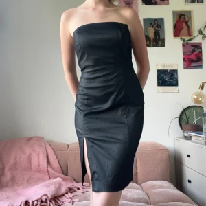 Svart bandeauklänning Mexx - Snygg svart axelbandslös klänning från Mexx med figurnära passform och slits framtill. Klänningen är kort och har dragkedja i sidan. 