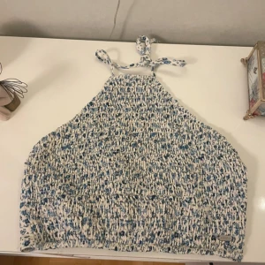 Blommig linne/topp med knytband - Supersöt linne/halternecktopp med blått blommönster på vit botten. Toppen har smockad framsida, tunna knytband i nacken och knytning i ryggen för en snygg passform. Perfekt för varma dagar och ger en romantisk vibe.💞
