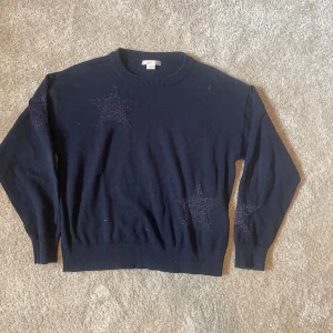 Mörkblå stickad tröja med stjärnor Gina Tricot - Mörkblå stickad tröja från Gina Tricot med glittriga stjärnor på bröstet, ärmen och ryggen. Tröjan har rund halsringning och långa ärmar. Perfekt för dig som gillar en chill men ändå snygg look.