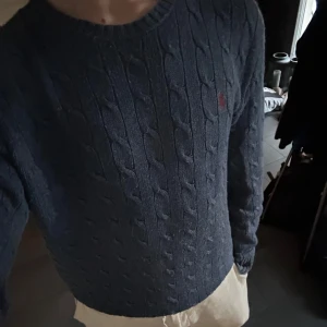 Kabelstickad Ralph Lauren Tröja - Blå (Stl M) - Säljer denna snygga kabelstickade tröja från Ralph Lauren. Tröjan är i ganska bra skick men har lite noppror samt är lite blek vid armbågarna. Nypris för tröjan ligger på ca 2200kr