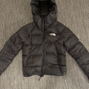 Svart pufferjacka från The North Face XS - Säljer en svart pufferjacka från The North Face i storlek XS (hyalite down hooded jacket). Jackan har huva, dragkedja framtill och två sidofickor med dragkedja. Klassisk logga på bröstet och ryggen. Säljer den då den inte kommer till användning.