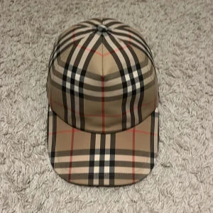 Burberry rutig keps i beige och svart - Snygg keps från Burberry med klassiskt rutigt mönster i beige, svart, vitt och röda linjer.