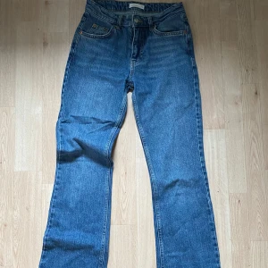 Blå bootcut jeans med hög midja - Snygga blå jeans med bootcut-modell och hög midja. Klassisk femficksdesign och raka ben som släpper ut lite nertill. Jeansen är i ett klassiskt blått denimtyg och passar perfekt till sneakers eller boots.