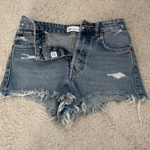 Blå jeansshorts från Zara - Snygga blå jeansshorts från Zara med råa, fransiga kanter och slitna detaljer framtill och baktill. Klassisk femficksmodell med medel hög midja och knappgylf. Aldrig använda men köpta förra sommaren 