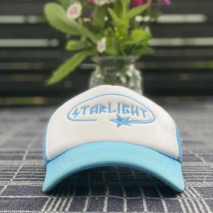 Starlight blå och vit keps - Snygg keps med broderad texten 'Starlight' och en stjärna framtill. Framsidan är vit med ljusblå detaljer och skärm, samt mesh i ljusblått på sidorna. Perfekt accessoar för en cool och avslappnad stil. Obs! Små fläckar på det vita, bör gå bort med vanish. Hör av dig vid ev frågor :)