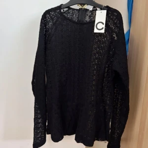 Svart spetsblus med lång ärm - Supersnygg svart blus i spets med lång ärm och rund hals. Blusen har ett detaljerat spetsmönster och är lätt transparent, perfekt för att lyfta din outfit. Sitter skönt och har en feminin vibe med fina detaljer.