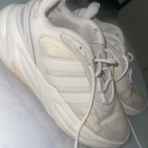 Sneakers från Adidas - Snygga chunky sneakers från Adidas i helvitt med klassiska tre ränder på sidan. Ovandelen är i mesh och syntet med detaljer i mocka. Tjock, mönstrad sula och snörning framtill. Perfekta för dig som gillar en sportig och trendig look. Har lite skador på tyget inne i skorna som ni kan se på bilderna ( inga synliga)