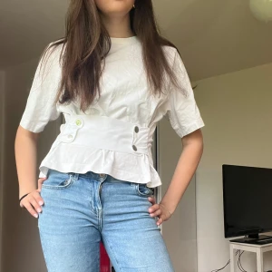 Vit t shirt med spänne över magen  - Säljer en vit t shirt med spänne över magen från lager 157