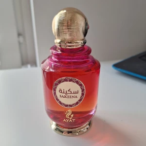 Sakeena parfym från Ayat 100 ml - Sakeena parfym från Ayat i en snygg rosa-röd glasflaska med guldfärgat lock. Doften har fräscha toppnoter av mandarin och passionsfrukt, hjärtnoter av apelsinblom, ros, havssalt och hallon samt basnoter av vanilj, mysk och pralin. Perfekt för dig som gillar fruktiga och söta dofter. (Ca 2 ml taget)