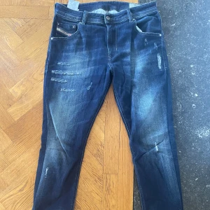 Mörkblå slitna jeans från Diesel - Snygga mörkblå jeans från Diesel med slitna detaljer och lätt tvättade partier. Klassisk femficksmodell med logotyp på myntfickan. Jeansen har en rak passform och är tillverkade i jeansmaterial med stretch för extra komfort. Storleken är 30/30 men sitter mer som 31/32 kanske lite mindre. Bara att hojta vid intresse. 