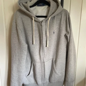 Polo Ralph Lauren - Huvtröja - Tja! Säljer en grå huvtröja med dragkedja från Polo Ralph Lauren. Den är i bra skick och har inga fel eller skador överhuvudtaget. Hör gärna av er vid funderingar!