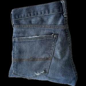 Ralph lauren jeans - Ralph lauren jeans  i blå denim med snyggt slitna detaljer och raka ben. Jeansen har fem fickor, knappgylf och tydliga kontrastsömmar. Perfekt för dig som gillar en tidlös och avslappnad look. I storlek 30/32