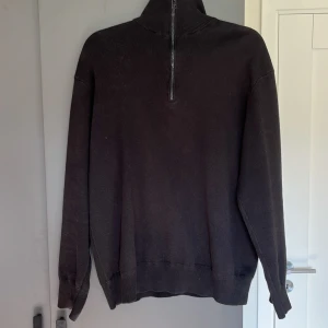 Svart stickad polotröja med half zip - Mörk, svart stickad polotröja med halv dragkedja framtill. Tröjan har lång ärm och ribbade muddar vid ärmslut och nederkant. Enkel och clean design som funkar till det mesta.