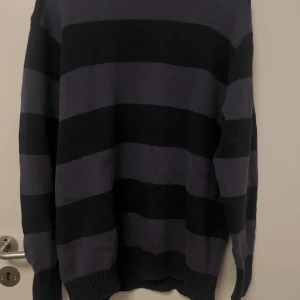Randig stickad tröja Brandy Melville - Mysig stickad tröja från Brandy Melville med breda svarta och mörkgrå ränder. Tröjan har lång ärm, rund halsringning och ribbade muddar. Perfekt för lager-på-lager och chill vibes.