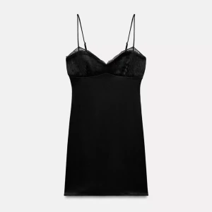 Svart kort klänning från Zara - Supersnygg svart kort klänning från Zara med tunna axelband och ribbad byst. Klänningen har spetsdetaljer vid urringningen och en slät, elegant kjoldel. Perfekt för dig som gillar stilren och trendig look.