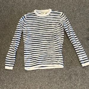 Randig stickad tröja från Dobber - Säljer en snygg stickad tröja från Dobber i vitt och marinblått med klassiskt randigt mönster. Tröjan har rund halsringning och långa ärmar, perfekt för dig som gillar en stilren och tidlös look. Passformen är normal och materialet känns mjukt och bekvämt.