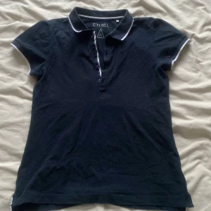 Mörkblå pikétröja från Etirel XS - Snygg mörkblå pikétröja från Etirel i storlek XS. Klassisk krage med vita ränder och knappar framtill. Tröjan har korta ärmar med vit kant och är gjord i mjuk bomull. Perfekt för en sportig och clean look. pris kan diskuteras. 