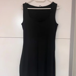 Svart ribbad långklänning - En svart, ärmlös långklänning med ribbad struktur och fyrkantig ringning. Klänningen har en enkel och stilren design som gör den lätt att styla. 