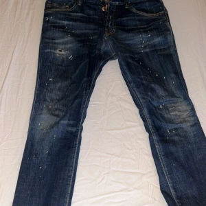 Dsquared2 blå jeans med färgstänk - Snygga blå jeans från Dsquared2 i klassisk femficksmodell. Jeansen har coola färgstänk och slitningar för en trendig, avslappnad look. Tillverkade i bomull med raka ben och kontrastsömmar. Perfekta för dig som gillar streetstyle och vill sticka ut. OBS! Pris kan diskuteras!