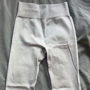 Ribbade träningstajts - Snygga ljusgrå tränibgstajts med ribbad struktur och bred, hög midja. Mjukt och stretchigt material som sitter skönt på kroppen. Perfekta för en chill vardagslook eller till träning. Diskret detalj på ena benet för extra stil.