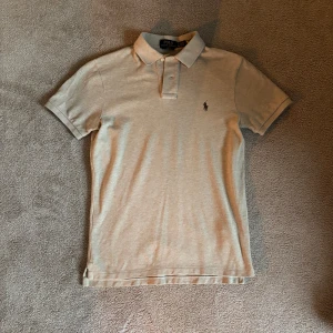 Beige pikétröja från Polo Ralph Lauren - Snygg beige pikétröja från Polo Ralph Lauren i slim fit-modell. Klassisk krage med knappar och den ikoniska broderade loggan på bröstet. Köpt från Zalando för ca 1300kr.
