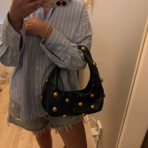 Cool Zara väska - Säljer nu min as snygga och coola populära väska ifrån Zara med guldiga nit detaljer i mörkgrön färg. Den är verkligen super fin men kommer tyvärr inte längre till användning. Knäpps med en magnet knapp och är hyfsat rymlig🥰