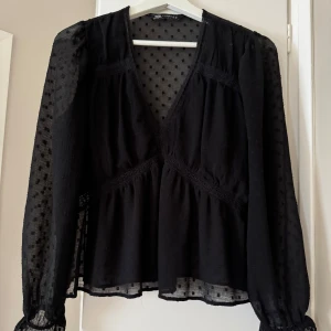 Svart prickig blus från Zara - Supersnygg svart blus från Zara med transparenta, långärmade ärmar och diskret prickigt mönster. Djup v-ringning och volangdetalj vid ärmslut. Lätt och luftig känsla, perfekt för att lyfta din outfit.💕