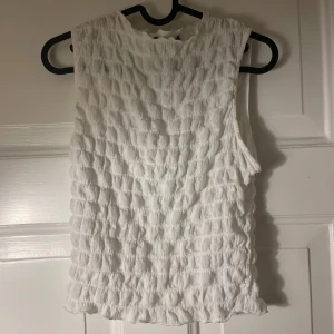 Vit ärmlös linnetopp Gina Tricot - Supersöt vit ärmlös linnetopp från Gina Tricot med strukturerad, bubblig yta. Toppen har rund halsringning och är perfekt att både klä upp och klä ner.