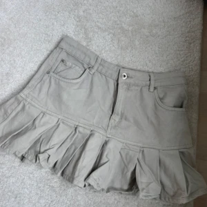 Beige volangkjol med jeanslook - Superfin beige kortkjol med volangkant och klassiska jeansdetaljer som fickor och bälteshällor. Kjolen har en avslappnad vibe och passar perfekt till sneakers eller boots. Materialet känns som bomull och ger en cool, casual känsla.