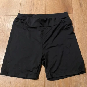 Svarta cykelshorts från SHEIN - Svarta cykelshorts från SHEIN i stretchigt och mjukt polyestermaterial. De har en bred midja och sitter skönt på kroppen, perfekta för träning eller chill. Enkla och stilrena utan detaljer eller mönster.