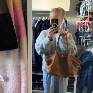 Brun mocka axelväska med långa handtag - Säljer en snygg brun axelväska i mjuk mocka med långa handtag. Väskan har en rymlig form och stilrena sömmar, perfekt för att bära allt du behöver. Enkel design utan synliga loggor eller mönster, passar till många outfits.