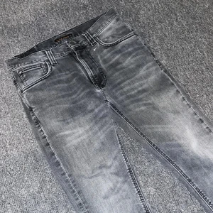 Grå jeans från Nudie Jeans - Snygga grå jeans från Nudie Jeans med en klassisk femficksdesign. De har en slim passform och är tillverkade i slitstarkt denim. Perfekta för en avslappnad stil med en touch av edge. Storlek w28, l28. 