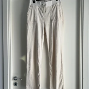 Vita mjukisbyxor Juicy Couture S - Vita mjukisbyxor från Juicy Couture i mjuk bomullsmix. Byxorna har snörning i midjan, stora fickor fram och bak med knappdetaljer samt broderad logga på ena fickan. Perfekta för en chill och trendig look. Några små fläckar finns men inget som stör. 