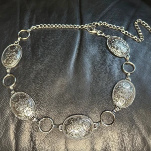 Nytt Silver Concho Belt Flowe Boho  -  Oanvänt bohoinspirerat statementbälte i silverfärgad metall. Klassisk concho-stil med blommiga ovala plattor – perfekt till både klänning, jeans eller festivaloutfit. Bältet är justerbart med kedja: minsta längd ca 63 cm, max ca 103 cm. Varje platta är drygt 4 cm bred. Ingen prutning – men jag erbjuder alltid rabatt vid köp av flera saker. Kika gärna på mina andra annonser! 