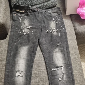 Svarta jeans Supply & Demand - Svarta jeans från Supply & Demand med slitna detaljer, trasiga partier och blekta effekter. Modellen har dragkedja vid fickan och en smal passform. Materialet är 93% bomull, 5% polyester och 2% elastan för stretch och komfort.