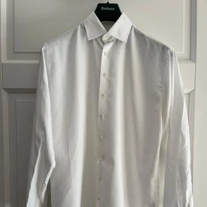 Vit skjorta i strykfri bomull - Klassisk vit skjorta från Herr Karl of Sweden i strykfri bomull. Skjortan har lång ärm, snygg krage och knappar framtill. Tyg med diskret fiskbensmönster och manschett för manschettknappar. Perfekt för dig som vill ha en clean och stilren look.
